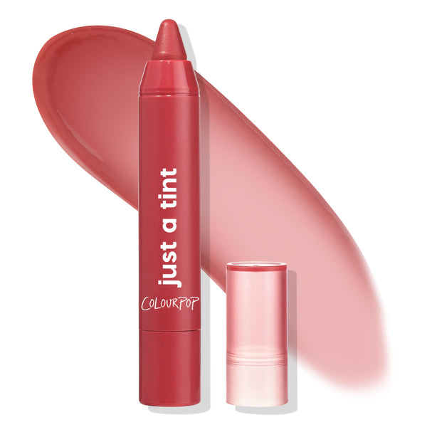 A Go Go ColourPop Lip Tint crayon uncapped and standing, showing a warm coral-red tip, with a translucent pink cap beside it and a glossy matching swatch behind, just a tint branding visible on a white background.