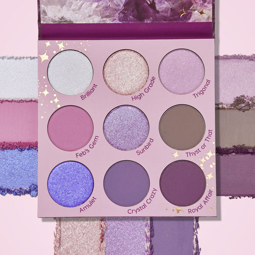 ColourPop All Amethyst shadow palette displays a 9-pan array of purple-toned shades - icy silver, lilac shimmers, taupe, and matte plums - with swatches framing the compact on a pink backdrop and an amethyst-print lid.