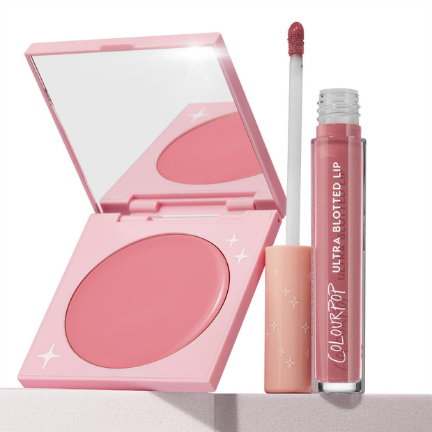 That’s So Rosy ColourPop Cheek & Lip Set showcasing an open pink compact cream blush beside an Ultra Blotted Lip tube with doe-foot applicator, both in rosy mauve tones, styled on a light pedestal against a clean white background with star-accent packaging.
