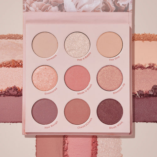 Blush Crush ColourPop Shadow Palette lies open, displaying a 9-pan range of rosy nude mattes and shimmers - Lovesick, Pop a Bottle, The One, Enamored, Made U Blush, Blossom Up, How Rouge, Cheek2Cheek, Blush Wine - with swatches streaked across a blush-pink backdrop.