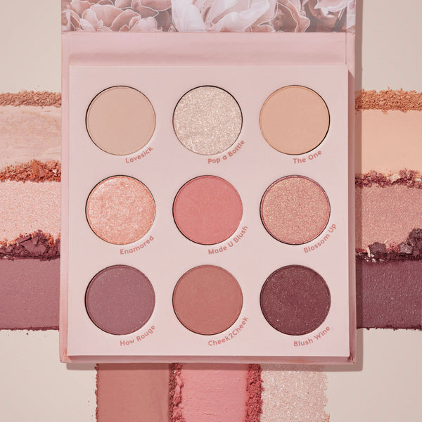 Blush Crush ColourPop Shadow Palette lies open, displaying a 9-pan range of rosy nude mattes and shimmers - Lovesick, Pop a Bottle, The One, Enamored, Made U Blush, Blossom Up, How Rouge, Cheek2Cheek, Blush Wine - with swatches streaked across a blush-pink backdrop.