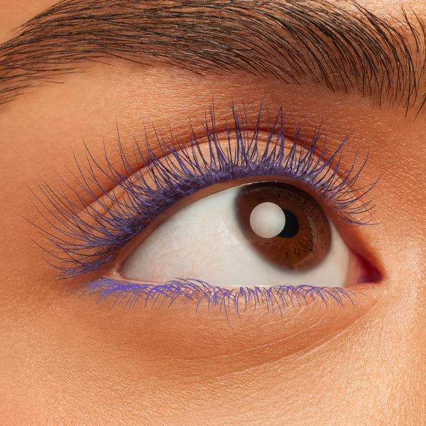 Brown eye showcasing lashes coated in ColourPop BFF Mascara, shade Purple Prose, lengthening and defining with bold violet color while the lower lash line is lightly painted in purple, captured in an extreme close-up with natural brow and skin texture.