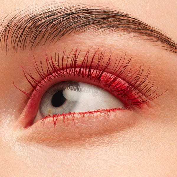 Red-coated eyelashes fan upward, wearing the Left on Red shade of the ColourPop BFF Mascara, in a tight close-up of an eye with clean skin and a groomed brow, emphasizing bold pigment and defined length.