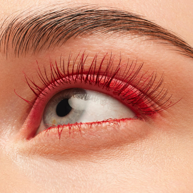 Red-coated eyelashes fan upward, wearing the Left on Red shade of the ColourPop BFF Mascara, in a tight close-up of an eye with clean skin and a groomed brow, emphasizing bold pigment and defined length.