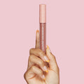 ColourPop Ultra Matte Lip in Beeper, a mauve‑nude liquid lipstick, held upright by a manicured hand with peach‑tipped nails; clear tube shows the shade and a peach cap with white stars against a soft pink background.