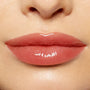 Glossy lips wearing ColourPop Lux Lip Oil in Bells, delivering a sheer peachy-rose tint and glass-like shine; smooth, non-sticky finish shown in a tight close-up of the lower face under soft studio lighting.