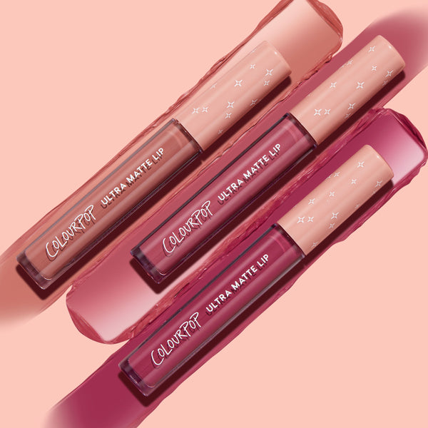Three ColourPop Ultra Matte Lip tubes from the Berry Pickin' Ultra Matte Lip bundle lie diagonally with matching nude, rose, and deep berry swatches on a pink backdrop; clear barrels and blush caps with white stars showcase the shades.