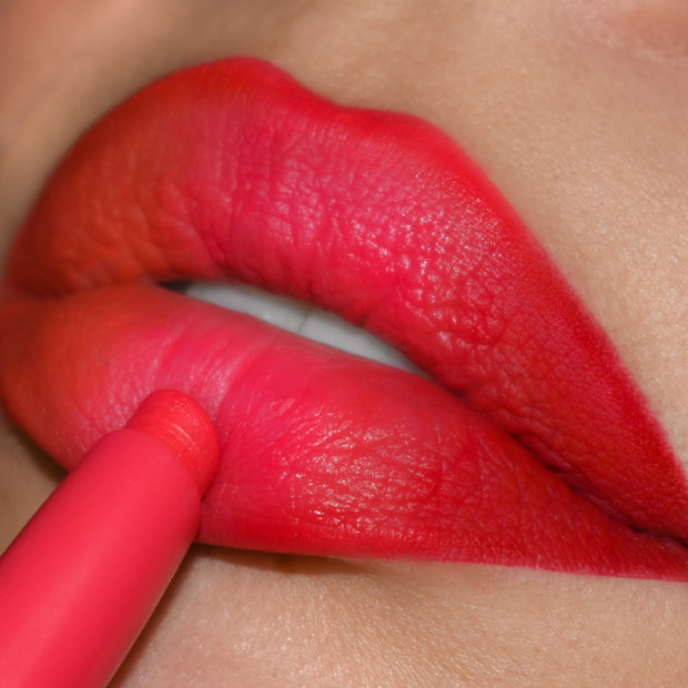 Chi Chi ColourPop Lippie Pencil lining lips, depositing bold coral‑pink, soft‑matte color; extreme close-up shows the pencil’s precision tip defining the cupid’s bow and lower lip for a crisp, saturated outline.