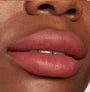 Lips wearing ColourPop Lippie Stix Brink, a warm rosy terracotta nude in a soft‑matte finish, shown in a close-up to highlight smooth, even coverage and creamy texture.
