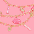 Brooklyn Charm x ColourPop Necklace showcasing gold link chains with playful charms - pink lips reading “ColourPop,” pink “So Juicy” tube tags, a gold bunny, and a jeweled strawberry - layered on a bright pink background.