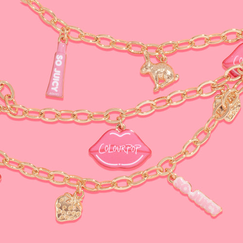 Brooklyn Charm x ColourPop Necklace showcasing gold link chains with playful charms - pink lips reading “ColourPop,” pink “So Juicy” tube tags, a gold bunny, and a jeweled strawberry - layered on a bright pink background.