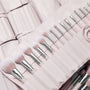 Stone Cold, a ColourPop Makeup Brush Kit, fanned in a blush-pink roll as face and eye brushes slot into stitched pockets, soft white-to-pink bristles and silver ferrules gleaming, with additional matching brush rolls layered behind.