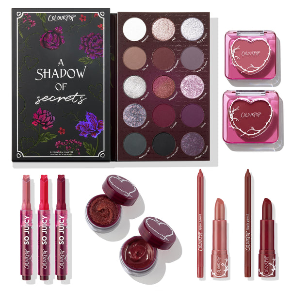 A Shadow of Secrets Collection ColourPop Full Collection Set displaying an open 15-shade eyeshadow palette in mauves, plums, and silver shimmers, two pink heart-embossed blush compacts, three So Juicy lip gloss sticks, two potted pigments, a lip pencil, and two lipsticks on white.