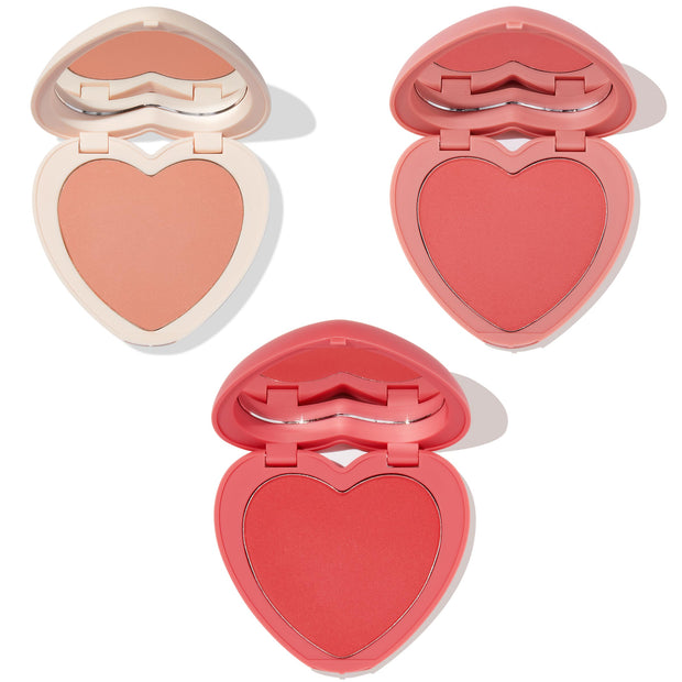 Three heart-shaped blush compacts showcase soft peach, warm coral, and vibrant rosy red pans with built-in mirrors on a white background; Cupid Called, a ColourPop Heart Powder Blush Set delivering buildable powder cheek color.