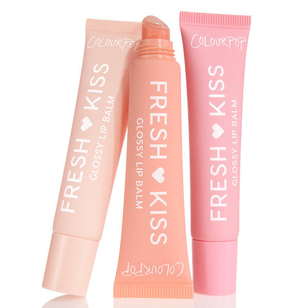 Pretty in Pastels ColourPop Glossy Lip Balm Trio showcases three Fresh Kiss glossy lip balms - soft pink, peach, and blush - with the center tube uncapped to show a slanted applicator, arranged upright on a white background.
