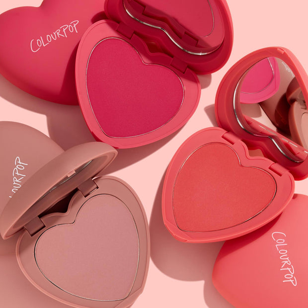 Totally Lovestruck ColourPop Heart Powder Blush Set features heart-shaped compacts opened to show hot pink, coral, and soft mauve powders with built-in mirrors and ColourPop logos, arranged on a blush-pink background.