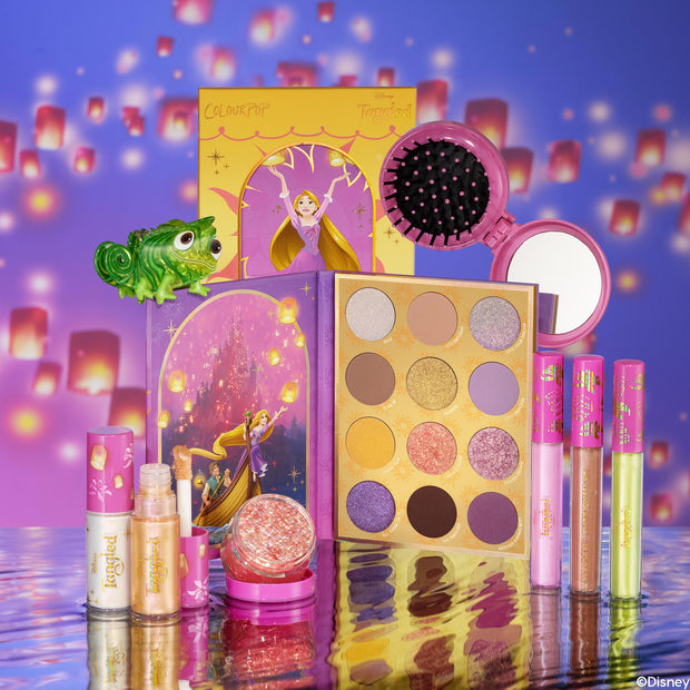 Disney Tangled and ColourPop Collection full set featuring Rapunzel-themed eyeshadow palette, lip glosses, highlighters, compact brush and mirror, and Pascal figurine arranged on reflective water-like surface with glowing lantern background, Back In Stock at ColourPop.