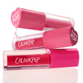 Tickle Me Pink ColourPop Lip Stain tubes stacked and gently dripping, showing vibrant rosy pink shades in clear barrels with hot pink caps stamped “hydra POP” and the ColourPop logo, styled on a bright white studio background.