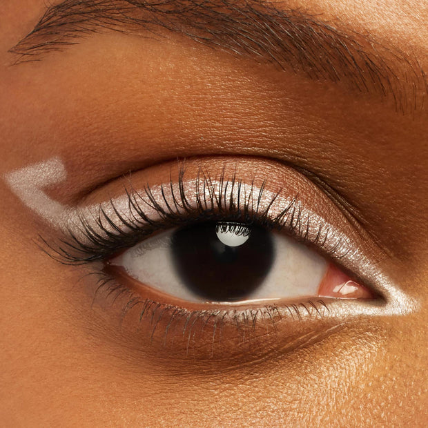 Graphic metallic silver eyeliner defines a close-up eye, with ColourPop Crème Gel Liner in Total Essentials tracing the upper lash line and inner corner and forming a sharp outer wing, shown on smooth warm-toned skin for a bold, precise look.