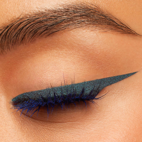 Metallic blue‑teal winged liner extends past the lash line on a closed eye, created with ColourPop Crème Gel Liner in Outer Space, showing a sharp cat-eye flick and defined lashes in a beauty macro close-up.