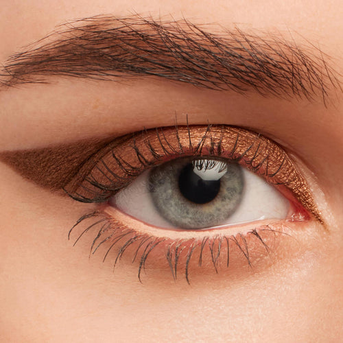 Metallic copper winged eyeliner on a gray-blue eye, showcasing Overboard, a ColourPop Crème Gel Liner; creamy bronze line sweeps across the upper lash line and extends to a soft flick, with a subtle lid smudge in a close-up beauty swatch.