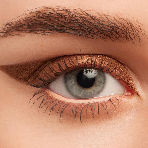 Metallic copper winged eyeliner on a gray-blue eye, showcasing Overboard, a ColourPop Crème Gel Liner; creamy bronze line sweeps across the upper lash line and extends to a soft flick, with a subtle lid smudge in a close-up beauty swatch.
