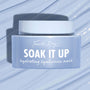 Fourth Ray Beauty Soak It Up Hydrating Mask jar shows “hydrating hyaluronic mask” as it rests on a glossy, water-swept pale blue surface; frosted periwinkle square container with white lid, a ColourPop Face Mask for dewy hydration.
