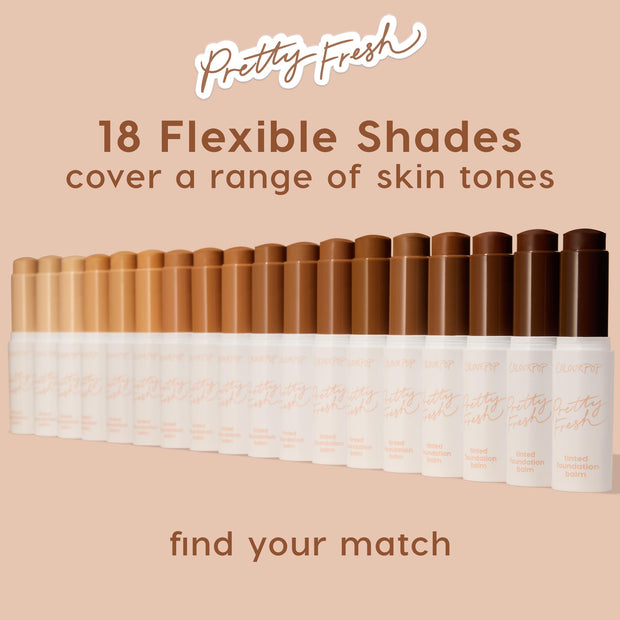 ColourPop Pretty Fresh Tinted Foundation Balm sticks lined up in a gradient of 18 flexible shades - from fair to deep - on a blush-beige backdrop, showcasing inclusive coverage; white tubes with peach script, including shades like Medium 12.