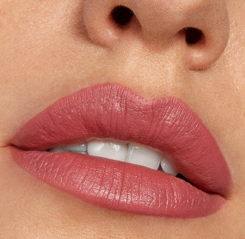 Lips wearing ColourPop Lippie Stix in Cami, a soft rosy mauve, show a full-coverage matte finish; slightly parted mouth reveals white teeth in a tight beauty close-up, highlighting smooth texture and crisp lip lines.