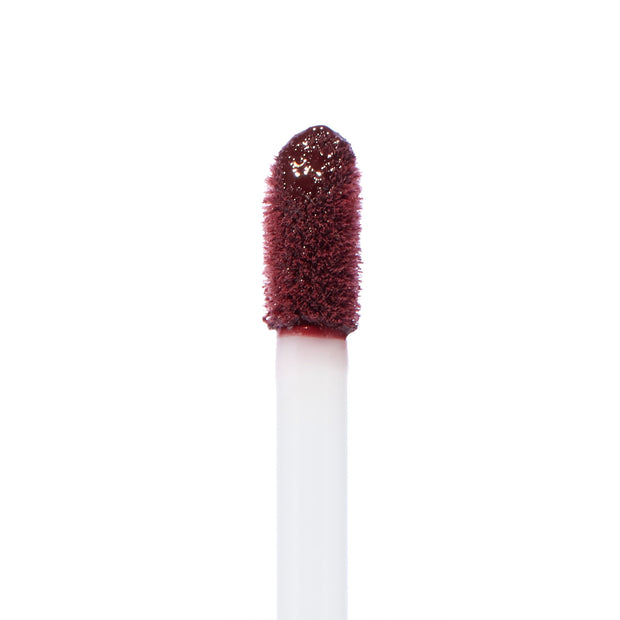 Doe-foot applicator coated in ColourPop Ultra Blotted Lip Canon Dr, a deep berry shade, captured in a macro close-up with saturated pigment on the fuzzy tip against a clean white background.