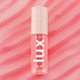 ColourPop Lux Lip Oil in Cherry Bite stands upright, displaying a clear pink-tinted tube with bold white LUX logo and a cream cap patterned with stars, set against glossy pink swirls that echo the coral lip oil tint.