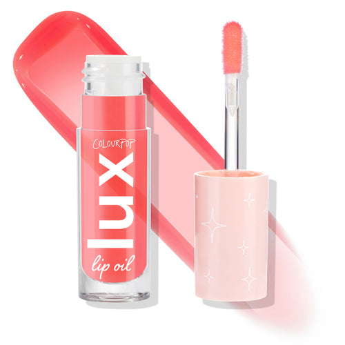 ColourPop Lux Lip Oil Cherry Bite stands open with doe-foot applicator and a glossy coral‑pink swatch, showing sheer tint and shine; clear square tube marked “lux,” pale pink cap with star motifs on a white backdrop.
