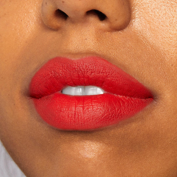 Full lips wearing Chi Chi Lippie Stix in bright coral-red with a soft matte finish, slightly parted to show teeth in a tight studio close-up; shade pairs well with a ColourPop Lippie Pencil for crisp definition.