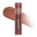 Cloudy Hour Cloud Whip Blurring Liquid Lipstick tube standing upright in front of a blurred swipe of warm matte nude color, showcasing the soft-focus Cloud Whip formula on a clean white background for US makeup shoppers.