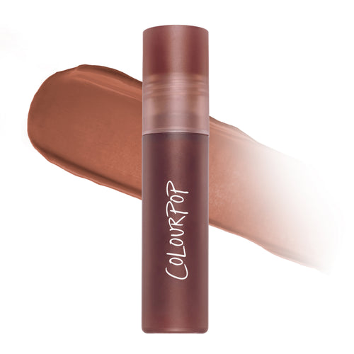 Cloudy Hour Cloud Whip Blurring Liquid Lipstick tube standing upright in front of a blurred swipe of warm matte nude color, showcasing the soft-focus Cloud Whip formula on a clean white background for US makeup shoppers.