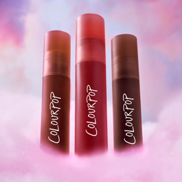 ColourPop Heavenly Nudes lip trio standing upright on fluffy pink clouds, each tube showing different nude lipstick shades in frosted gradient packaging, promoting beauty Value Sets against a dreamy pastel sky background.