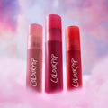 Three ColourPop Petal Plush lip trio tubes stand upright in fluffy pink clouds against a dreamy pastel sky, showcasing rich rosy and red shades as a colorful makeup value set for soft blurred lips.