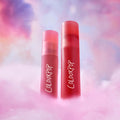 ColourPop Sunset Smooch Lip Ombre Duo standing upright as a red and pink liquid lipstick value set, rising from fluffy pink clouds against a dreamy pastel sky background.