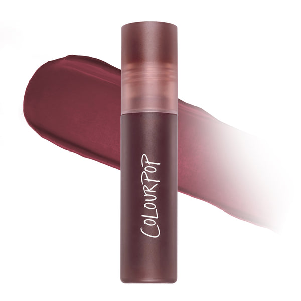 ColourPop Storm Cloud Cloud Whip Blurring Liquid Lipstick standing upright in a frosted mauve tube, shown against a blurred swatch of deep plum color on a white background, highlighting its soft-focus Cloud Whip finish.