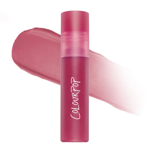 ColourPop What the Fluff Cloud Whip blurring liquid lipstick standing upright in a frosted pink tube, shown against a soft-focus swipe of rosy mauve pigment on a clean white background.