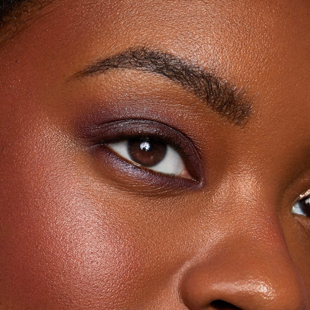 Close-up eyelid showcases ColourPop Bae Super Shock Shadow, a deep plum-purple eyeshadow softly blended from lash line to crease with a satin finish, defining the eye with a smoky wash against smooth, glowy skin.
