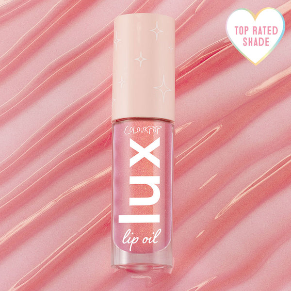 ColourPop Lux Lip Oil in Comb By shade standing upright, displaying a shimmery pink gloss in a clear tube with a blush cap and star accents, set against a rippled pink backdrop with a heart badge reading Top Rated Shade.