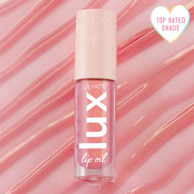 ColourPop Lux Lip Oil in Comb By shade standing upright, displaying a shimmery pink gloss in a clear tube with a blush cap and star accents, set against a rippled pink backdrop with a heart badge reading Top Rated Shade.