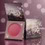 ColourPop Cream Blush in Obviously opens to show a rosy pink pan, with the Instant Crush box propped beside it; heart-and-bokeh graphics decorate the packaging on a reflective mauve backdrop.