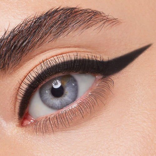 ColourPop Crème Gel Liner in Swerve draws a jet-black, precise cat-eye wing across the upper lash line of a blue eye, showcasing smooth, matte payoff and long-wear definition in a close-up beauty shot.