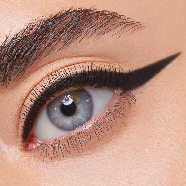 ColourPop Crème Gel Liner in Swerve draws a jet-black, precise cat-eye wing across the upper lash line of a blue eye, showcasing smooth, matte payoff and long-wear definition in a close-up beauty shot.