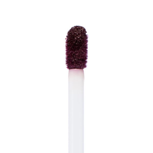 Doe-foot applicator coated in deep berry plum pigment, showing the saturated, velvety finish of ColourPop Ultra Matte Lip in Currant Mood, captured in a close-up macro against a clean white background.
