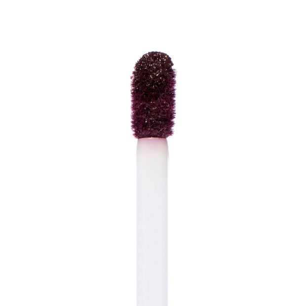Doe-foot applicator coated in deep berry plum pigment, showing the saturated, velvety finish of ColourPop Ultra Matte Lip in Currant Mood, captured in a close-up macro against a clean white background.