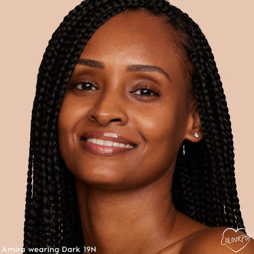 Model wearing Dark 19 N, ColourPop Pretty Fresh Tinted Moisturizer, smiling to showcase light, dewy coverage and an even, natural finish on deep skin tone; close-up with box braids on a soft beige background with ColourPop logo.