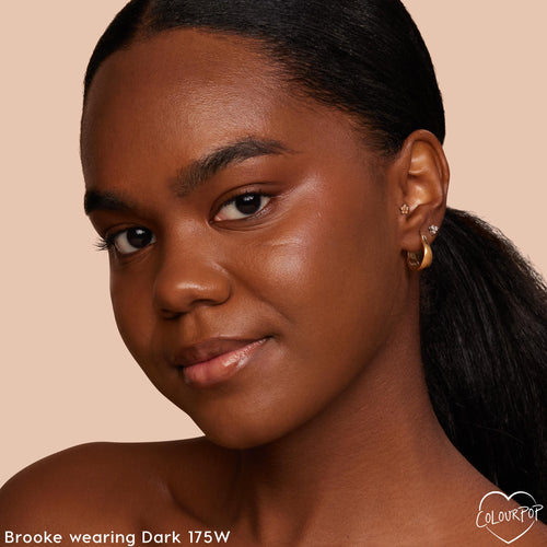 Model showcasing ColourPop Hyaluronic Hydrating Foundation in shade Dark 175 W, delivering smooth, dewy, even coverage; close-up portrait against a neutral backdrop with gold hoop earrings highlighting the skin-like finish.